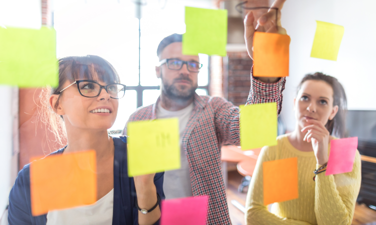 duas mulheres e um homem organizando post-its em mural transparente