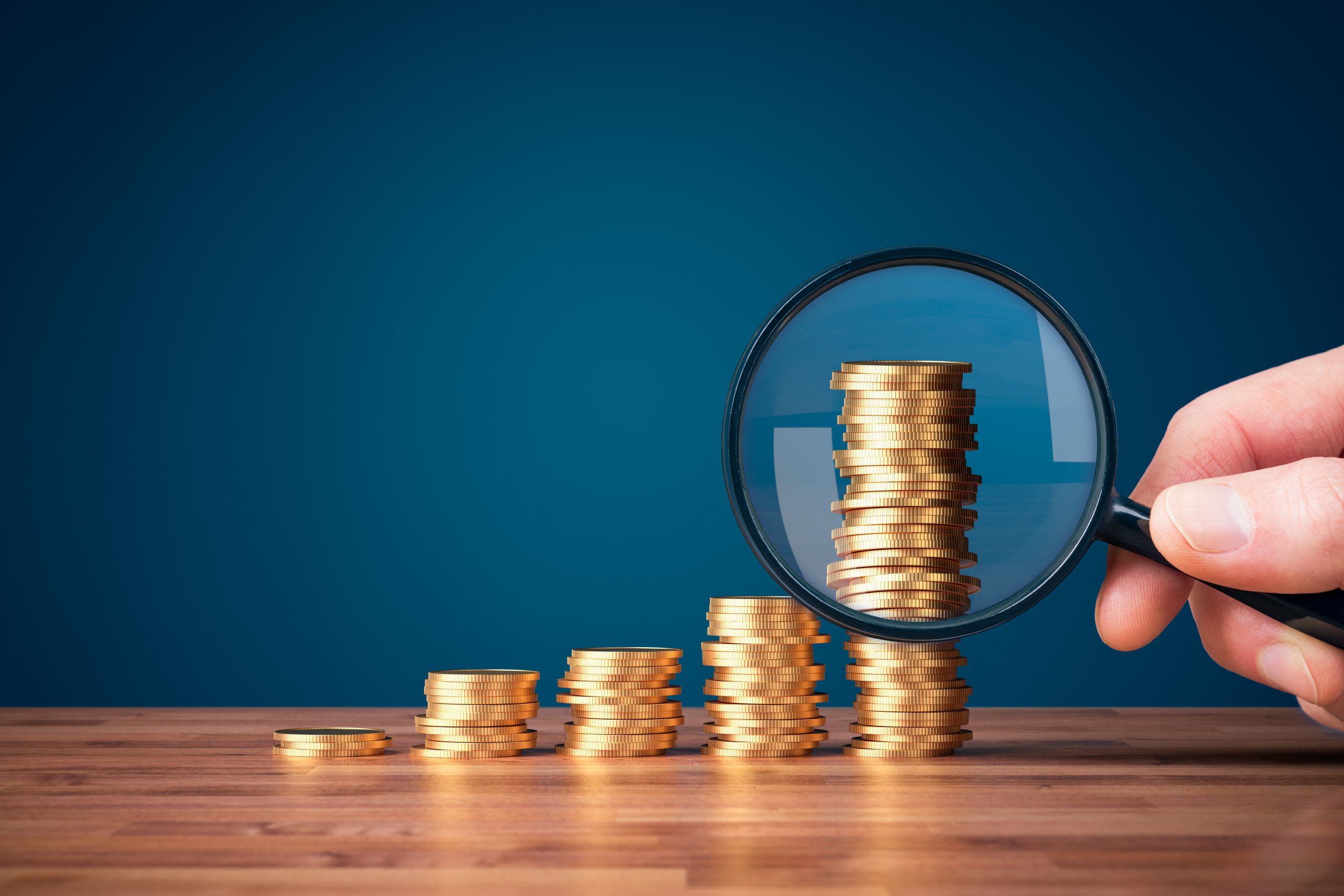 mão segurando um lupa apontando para moedas - gestão do fluxo de caixa