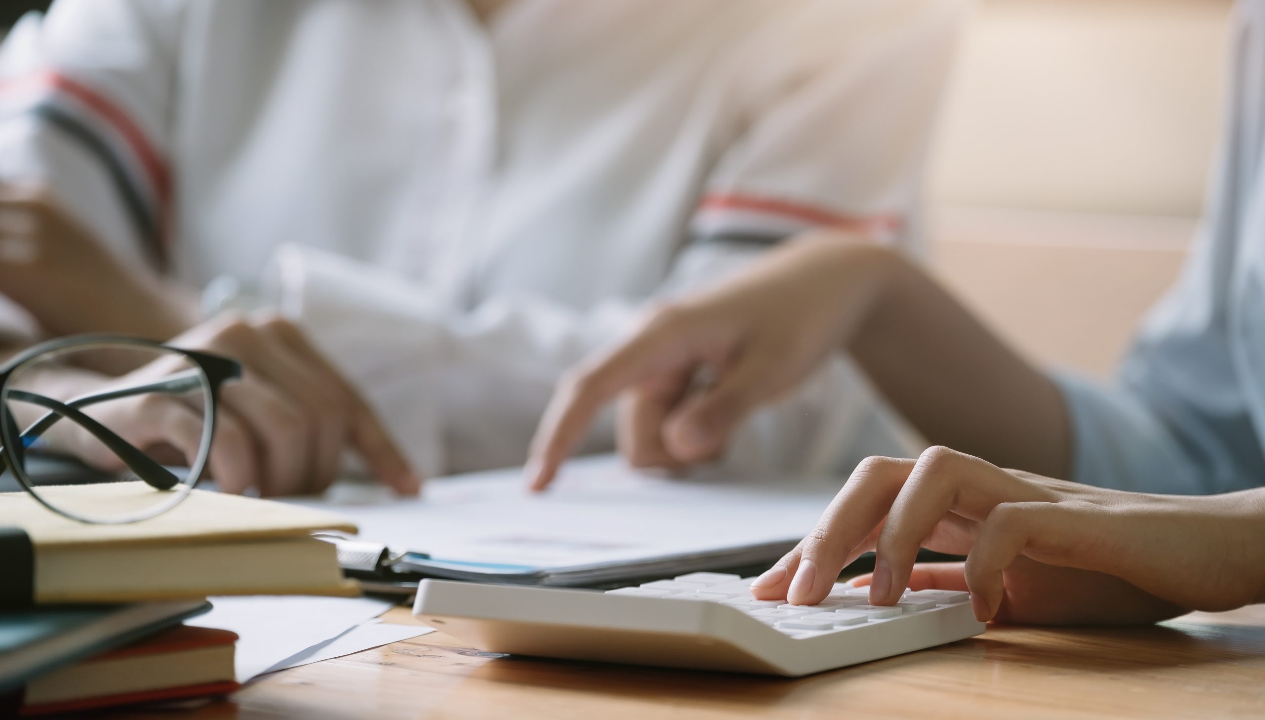caderno, livros e calculadora com duas pessoas com as mãos sobre uma mesa - quando contratar uma consultoria